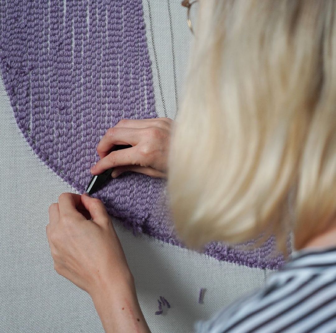 Antonia Eigel schneidet mit Schere Garn von handgetuftem Teppich ab